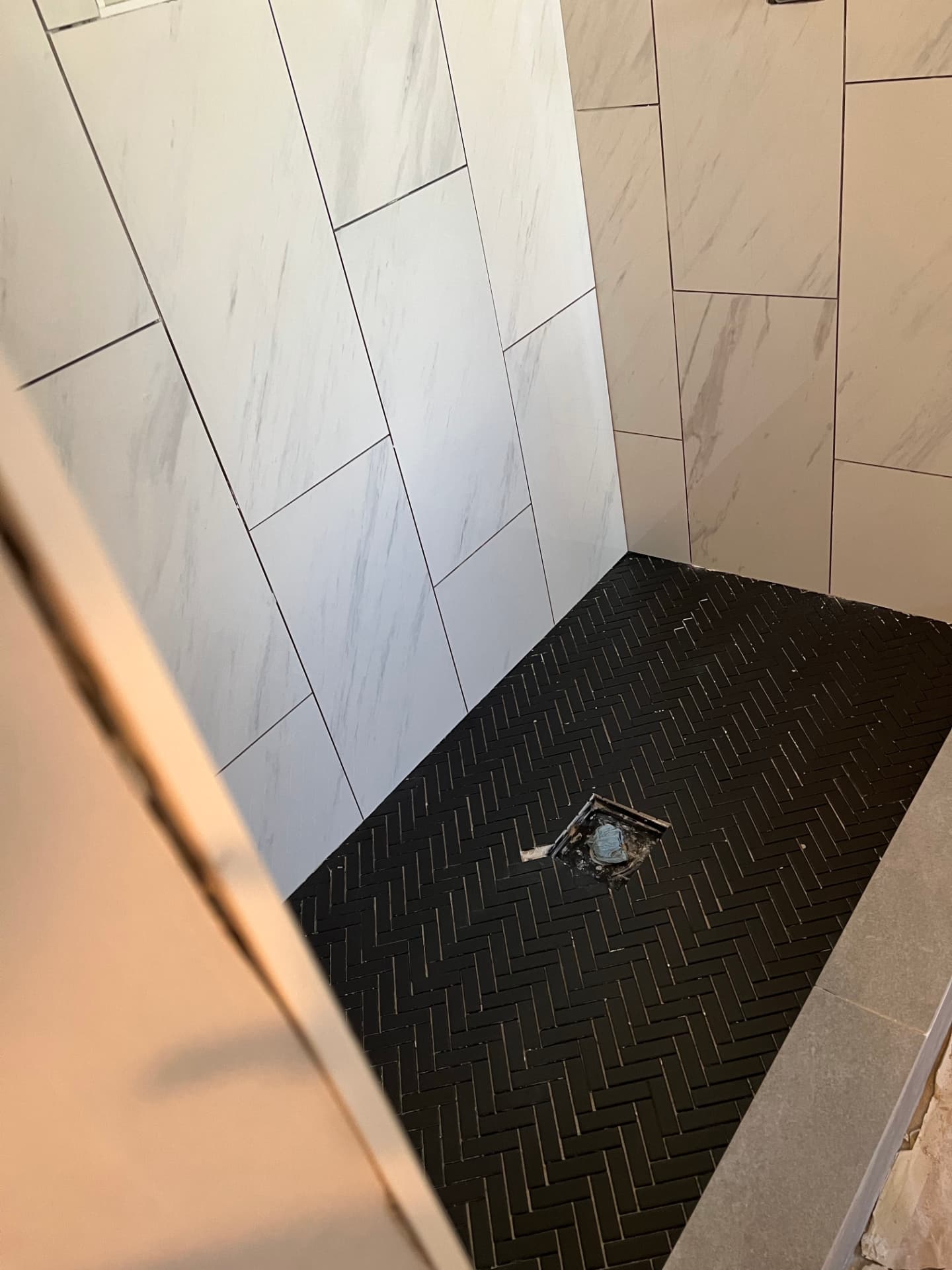 Bathroom shower renovation in progress with marble-look wall tile and black herringbone floor tile
