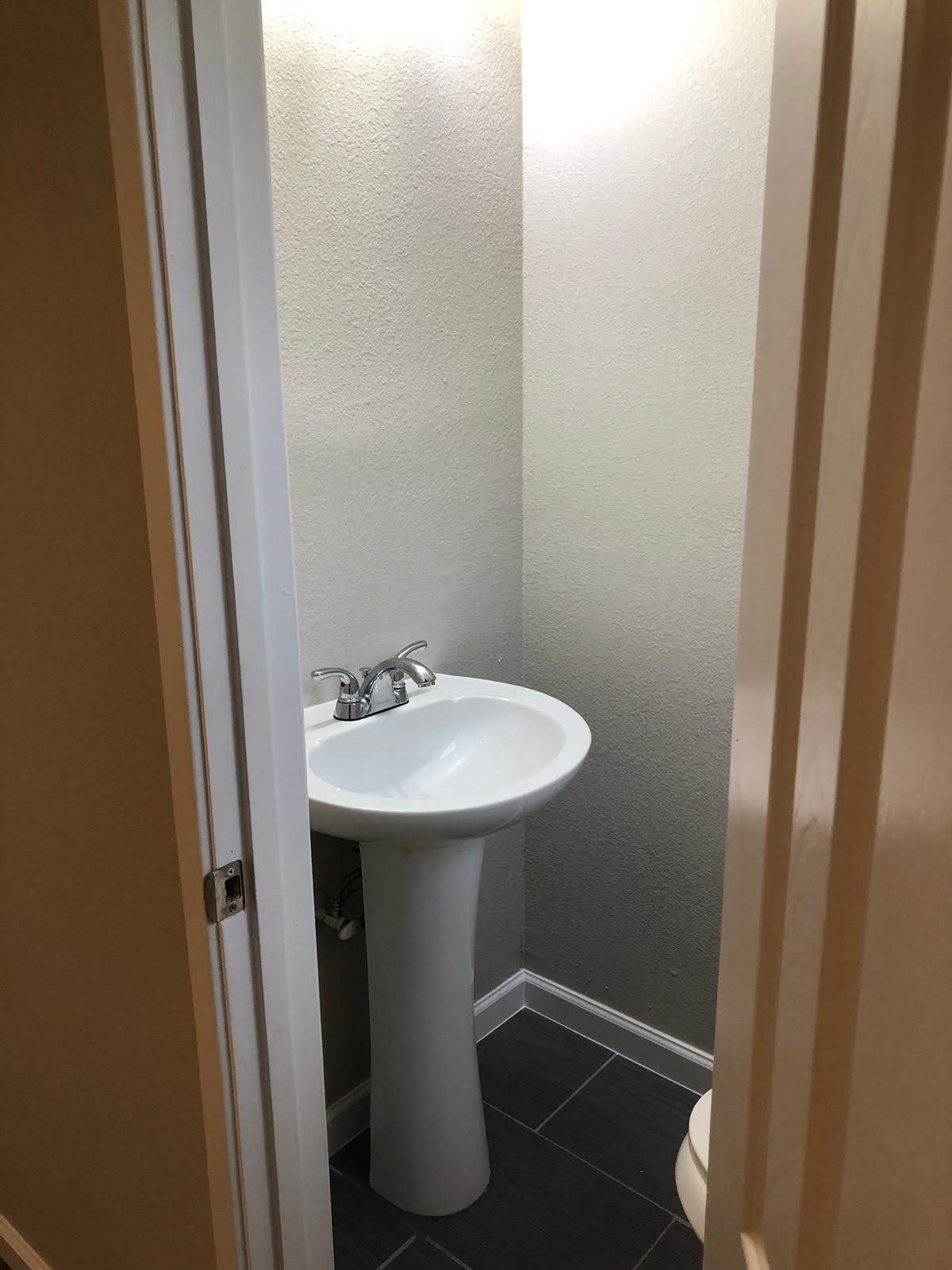Updated powder room with a white pedestal sink, gray walls, white trim, and dark floor tile