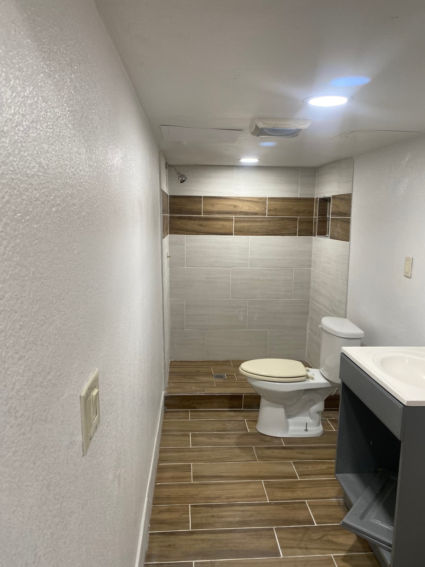 Finished bathroom upgrade with a tiled shower, wood-look floor tile, recessed niche, and dark vanity